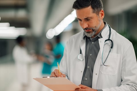 Focused doctor writing medical data on a clipboard in a clinic setting