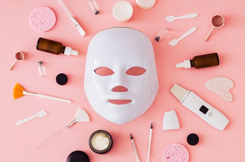Futuristic skincare technology composition with LED face mask and beauty tools on light pink background