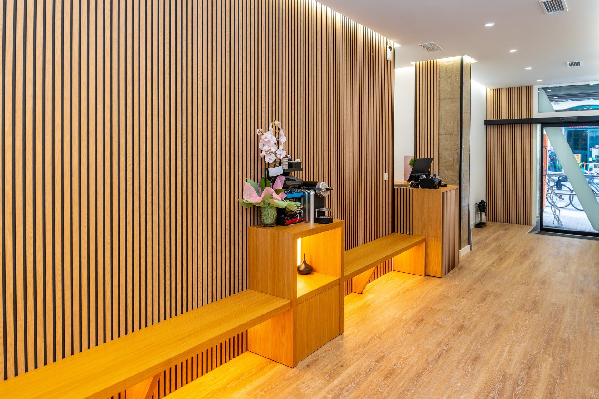 Aesthetic clinic interior showcasing a modern reception area with light wood slat walls, warm lighting, and minimalist furniture, creating a welcoming and sophisticated professional environment